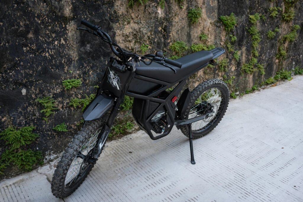 Modern black electric bike parked against a wall with green foliage on an urban street.